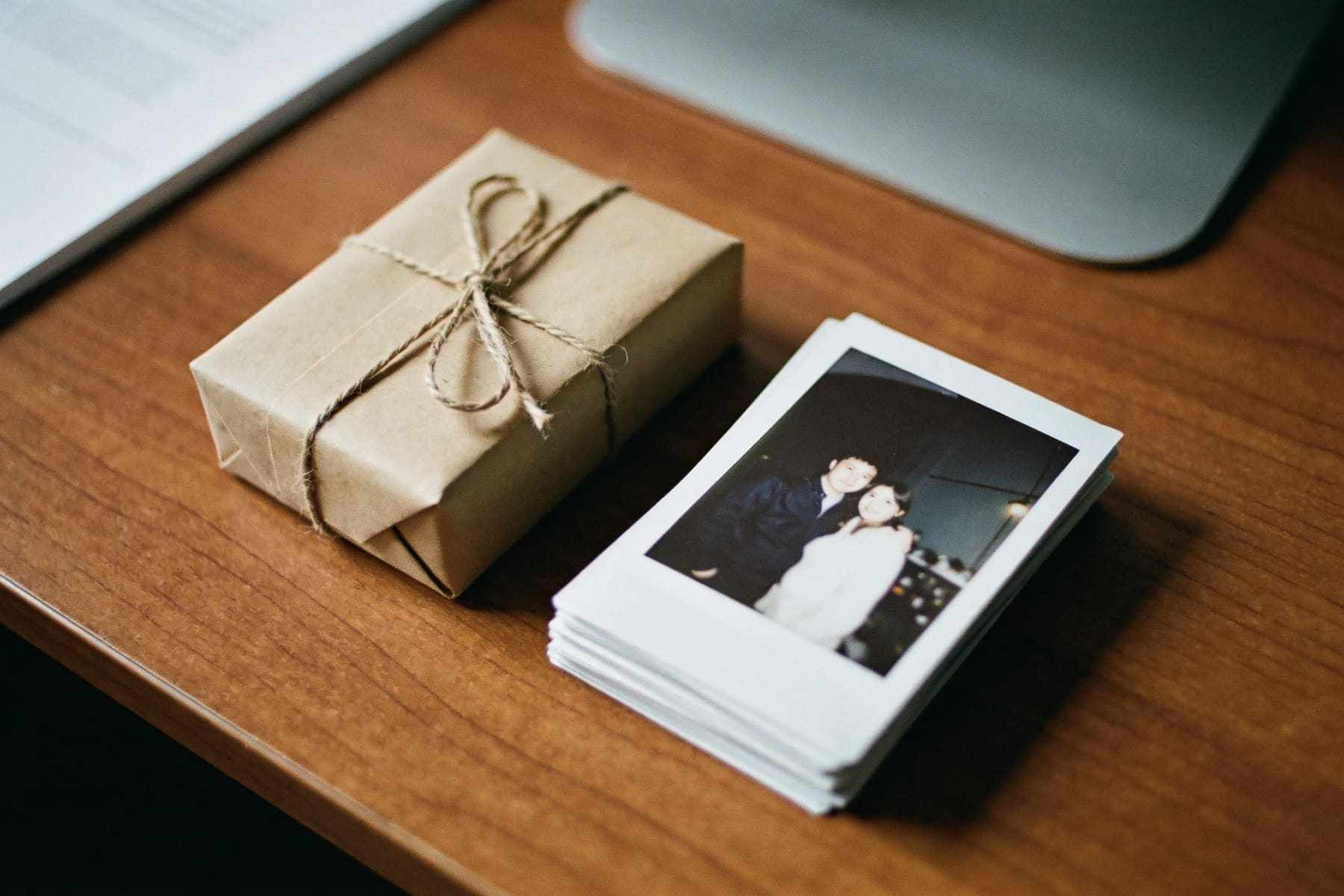 A small kraft paper gift envelope tied with string beside a stack of printed photos.