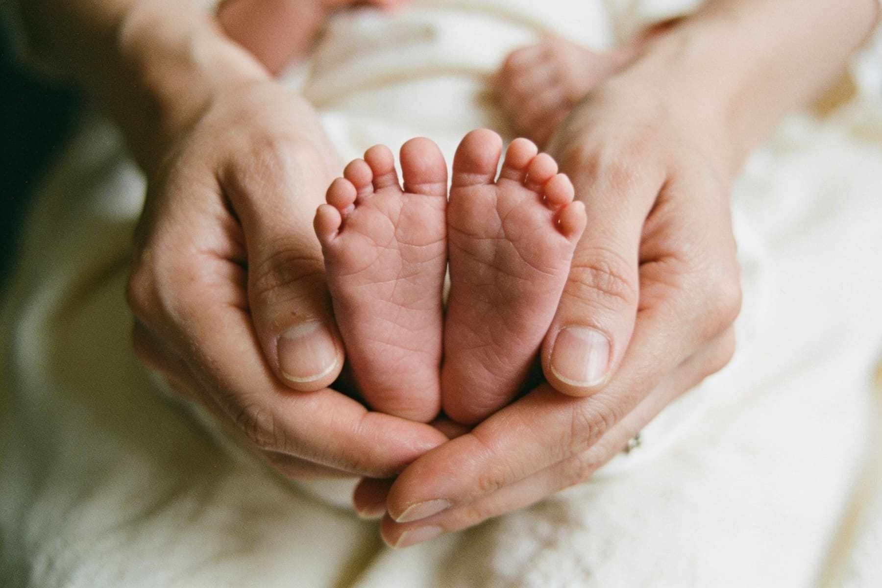 A newborn's tiny feet held in a parent's cupped hands.