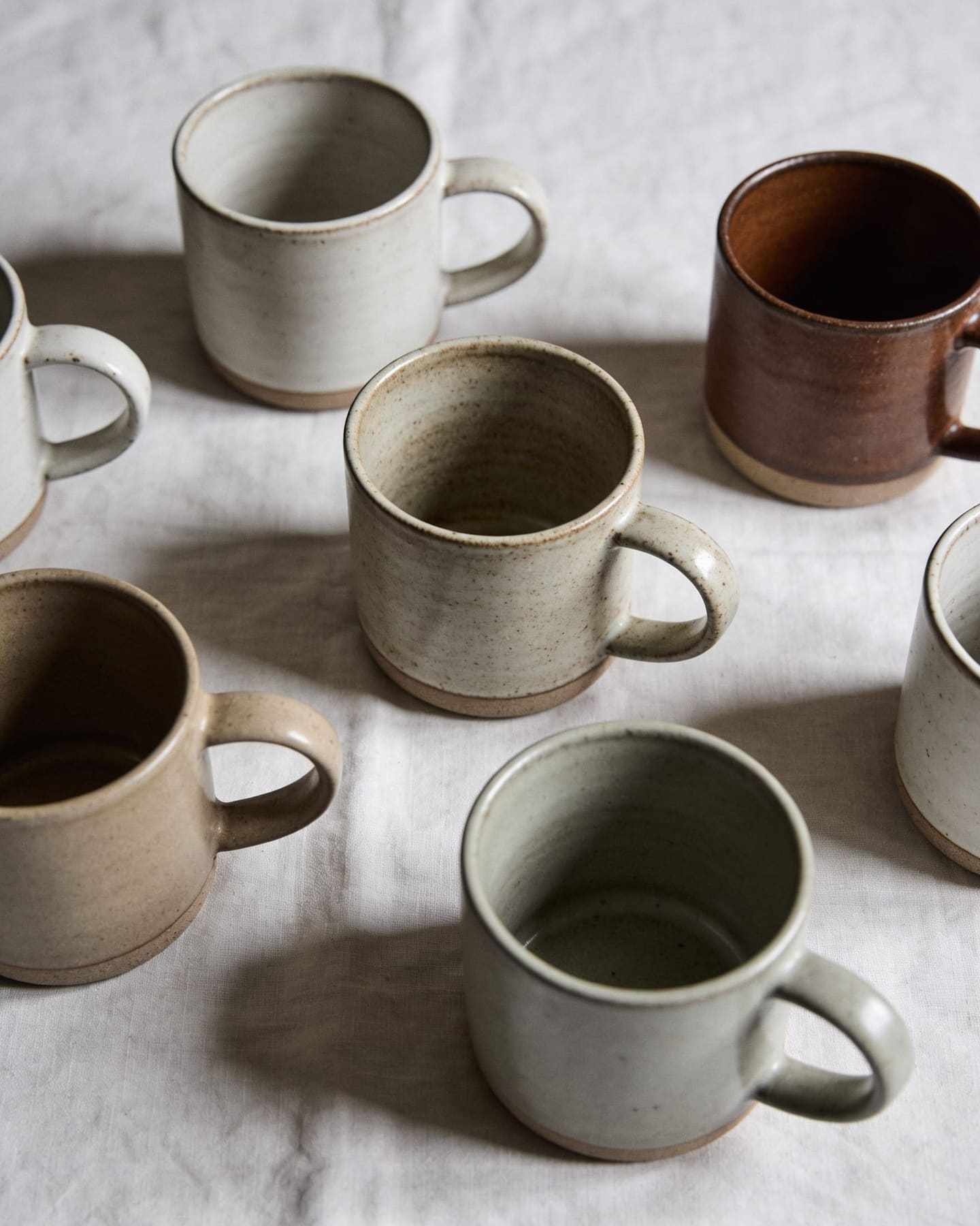 Handmade ceramic mugs in earthy glazes on a linen cloth in soft side light.
