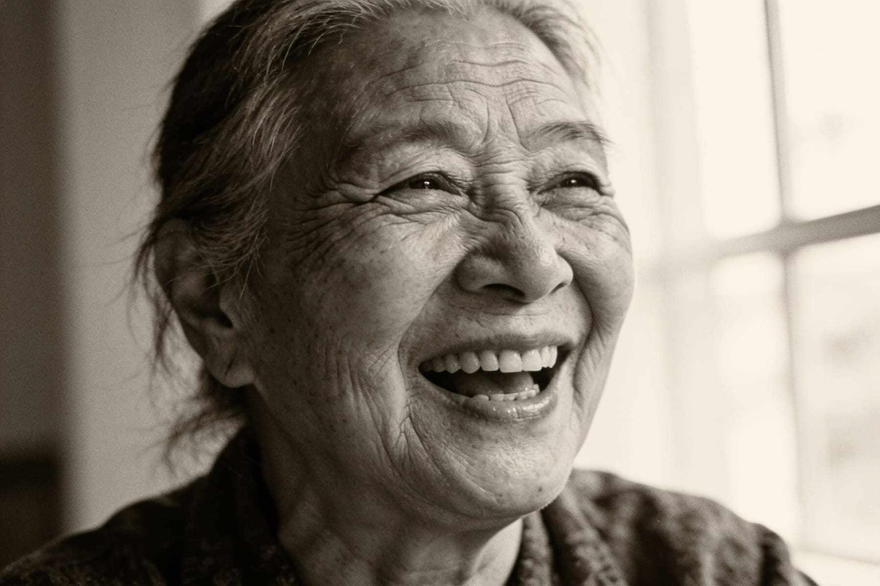 A black and white portrait of an elderly woman laughing.