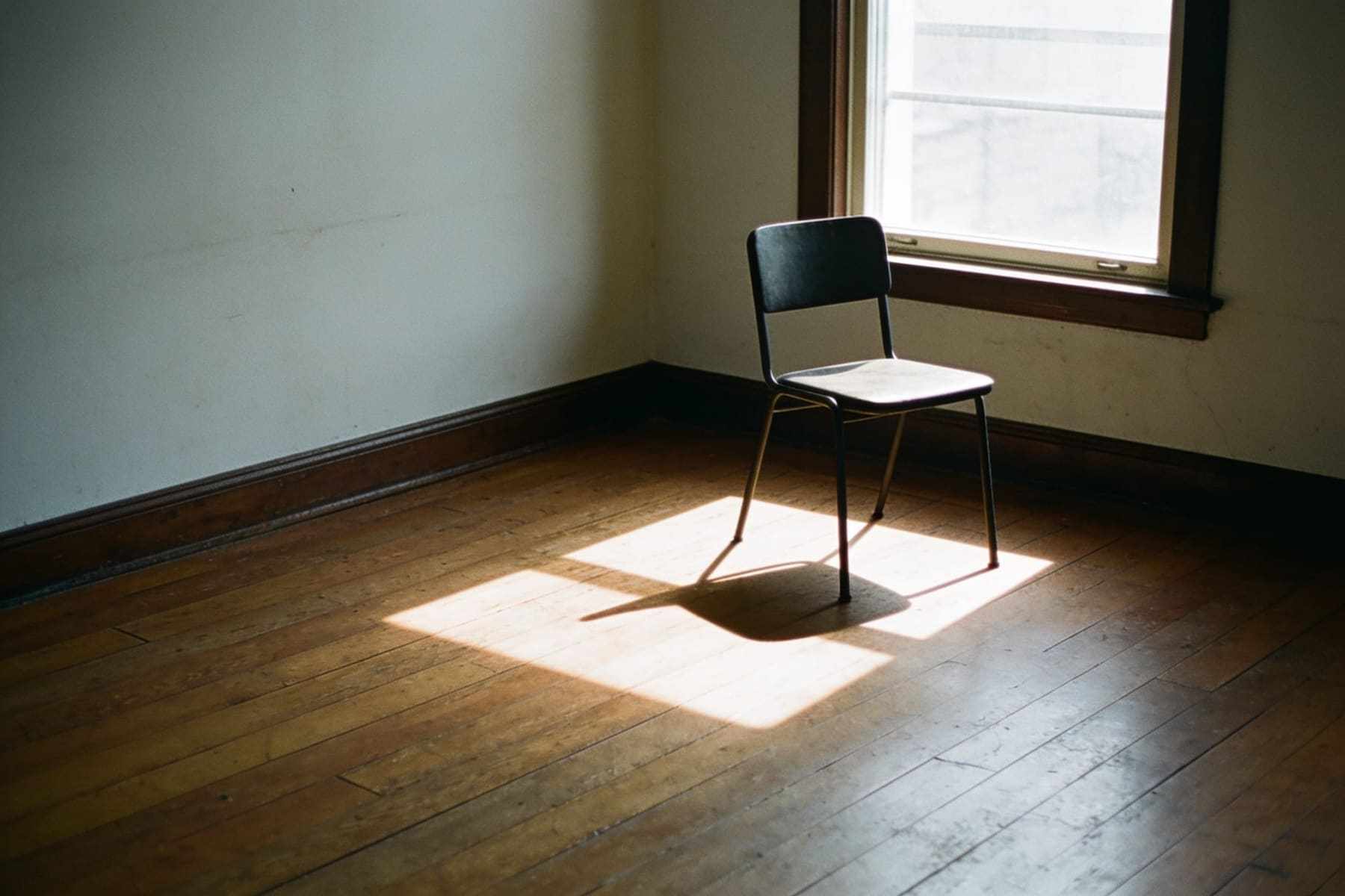 Soft window light falling across a wooden floor in a quiet room with a single chair.