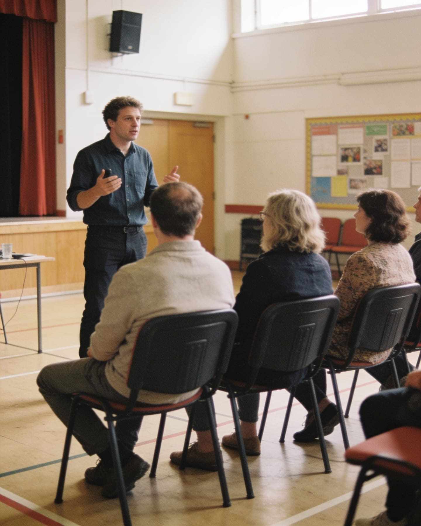 A speaker giving a talk to a small audience in a community hall.