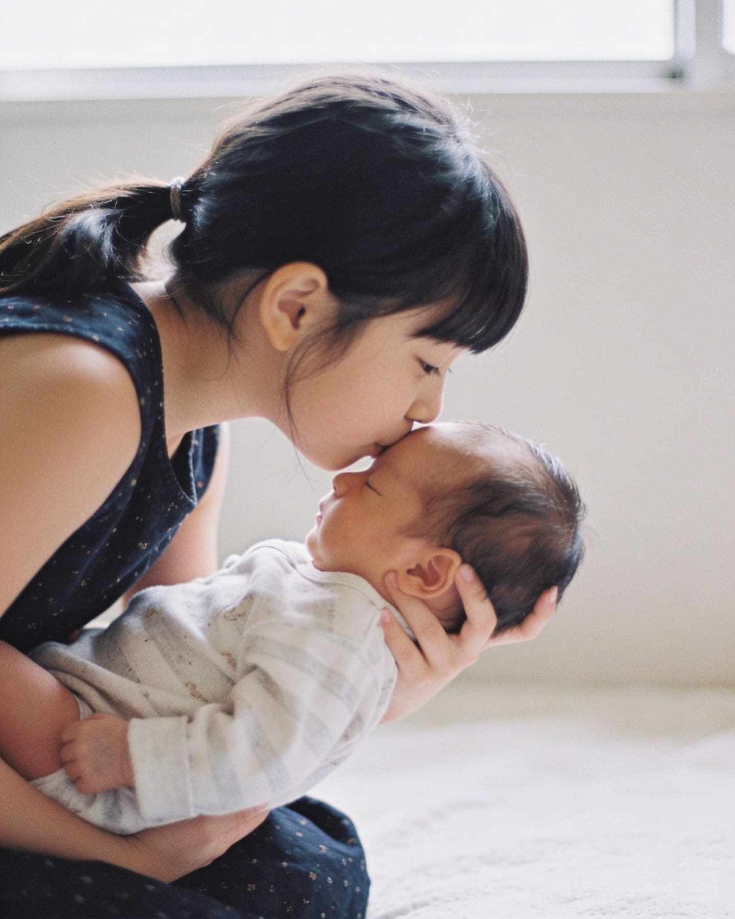 A big sister kissing her baby brother's forehead.
