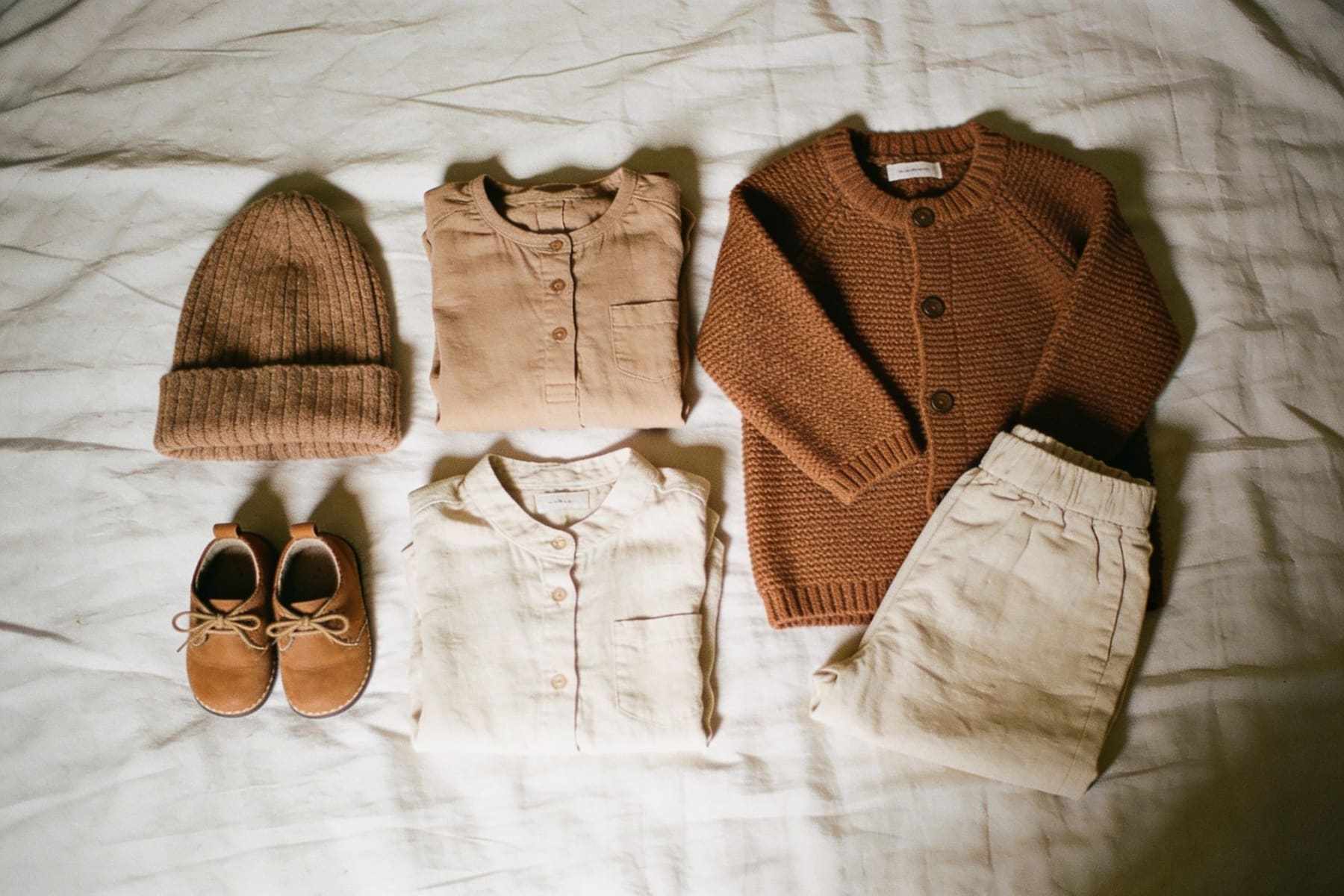 A flat lay of family outfits in muted earthy colours on a bed.